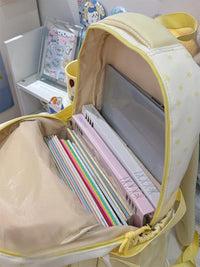 Backpack with stationery items including books and pens in a room setting.