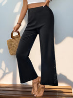 Person wearing black wide-leg pants with a white top and brown sandals, holding a woven bag.