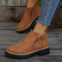 Brown suede ankle boots with zippers worn by a person on a wooden floor.