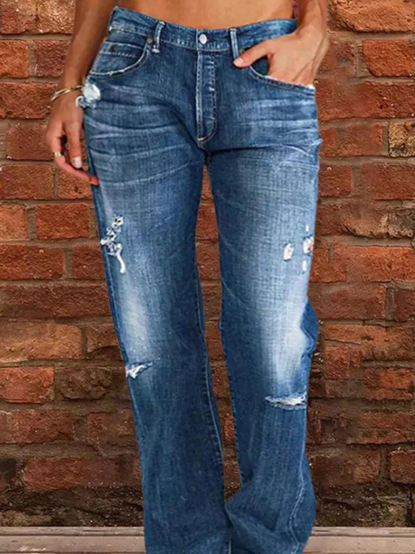 Person wearing distressed blue jeans against a brick wall.