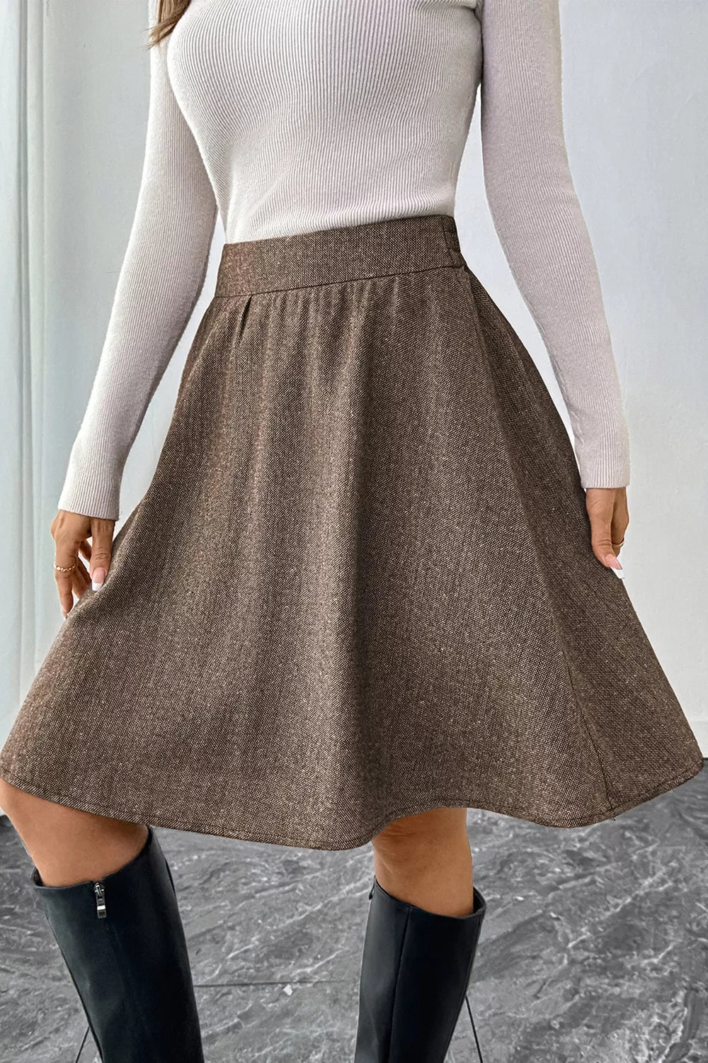 A brown A-line skirt with a textured, heathered finish, styled with a ribbed white long-sleeve top and black knee-high boots.
