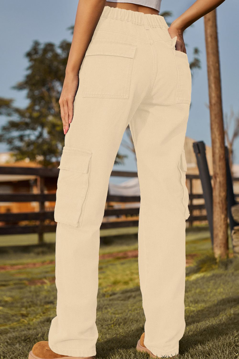 Beige pants worn by a person standing outdoors with a wooden fence and trees in the background.