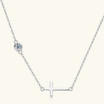 Silver necklace with a cross pendant and small round gem on a white background
