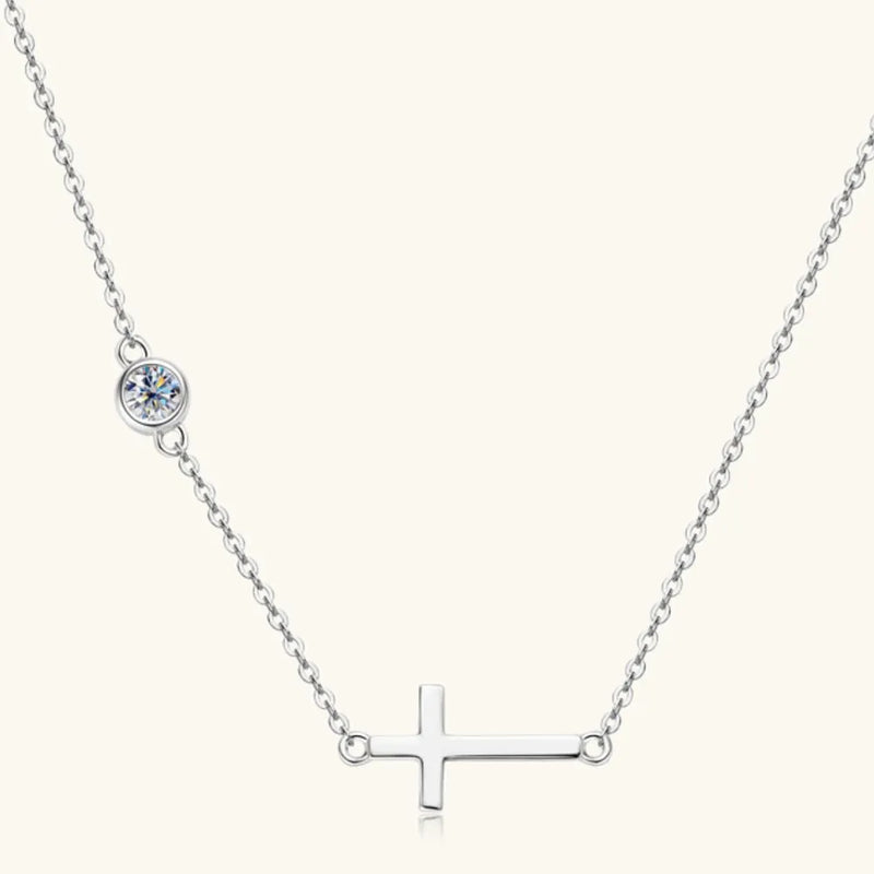 Silver necklace with a cross pendant and small round gem on a white background