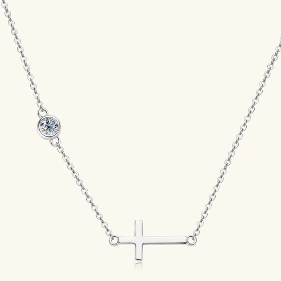 Silver necklace with a cross pendant and small round gem on a white background