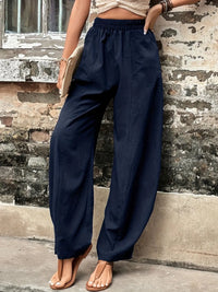 Person wearing navy wide-leg pants leaning against a textured wall.