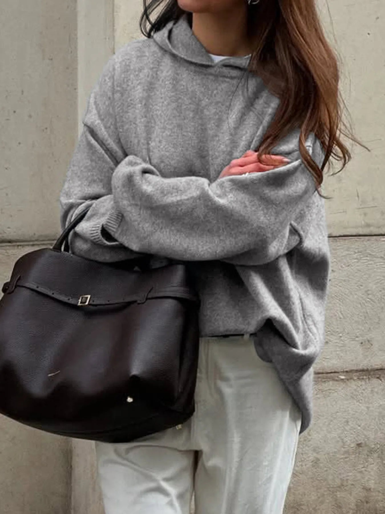Person wearing a gray oversized hoodie and holding a black bag against a neutral background