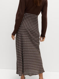 Person wearing a brown long-sleeve top and polka dot skirt on a white background