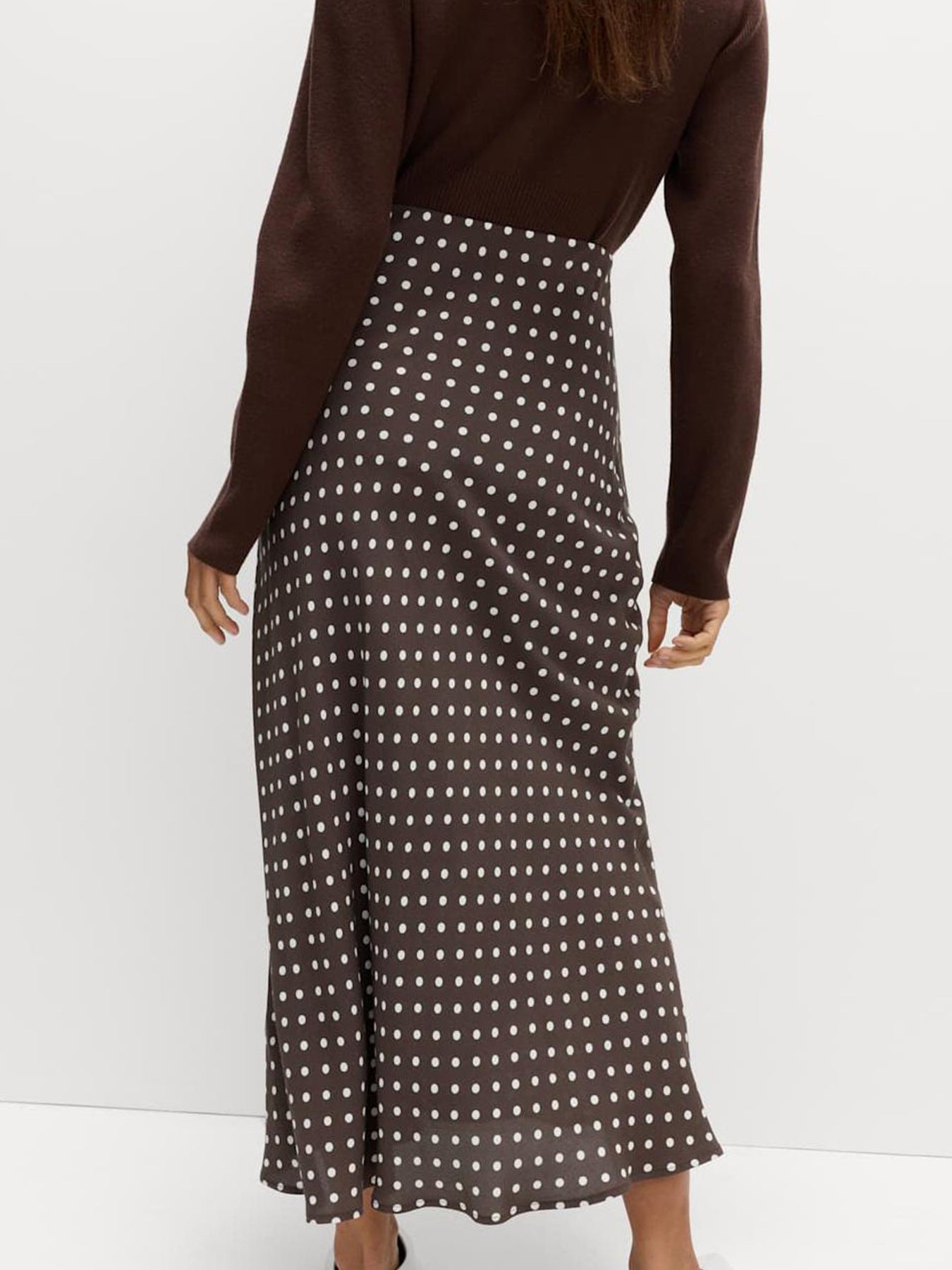 Person wearing a brown long-sleeve top and polka dot skirt on a white background