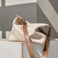 Beige handbag with brown strap on a light gray surface