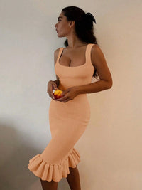 Woman wearing a peach-colored dress holding an orange against a neutral background
