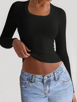 Person wearing a black long-sleeve top and blue jeans on a plain background