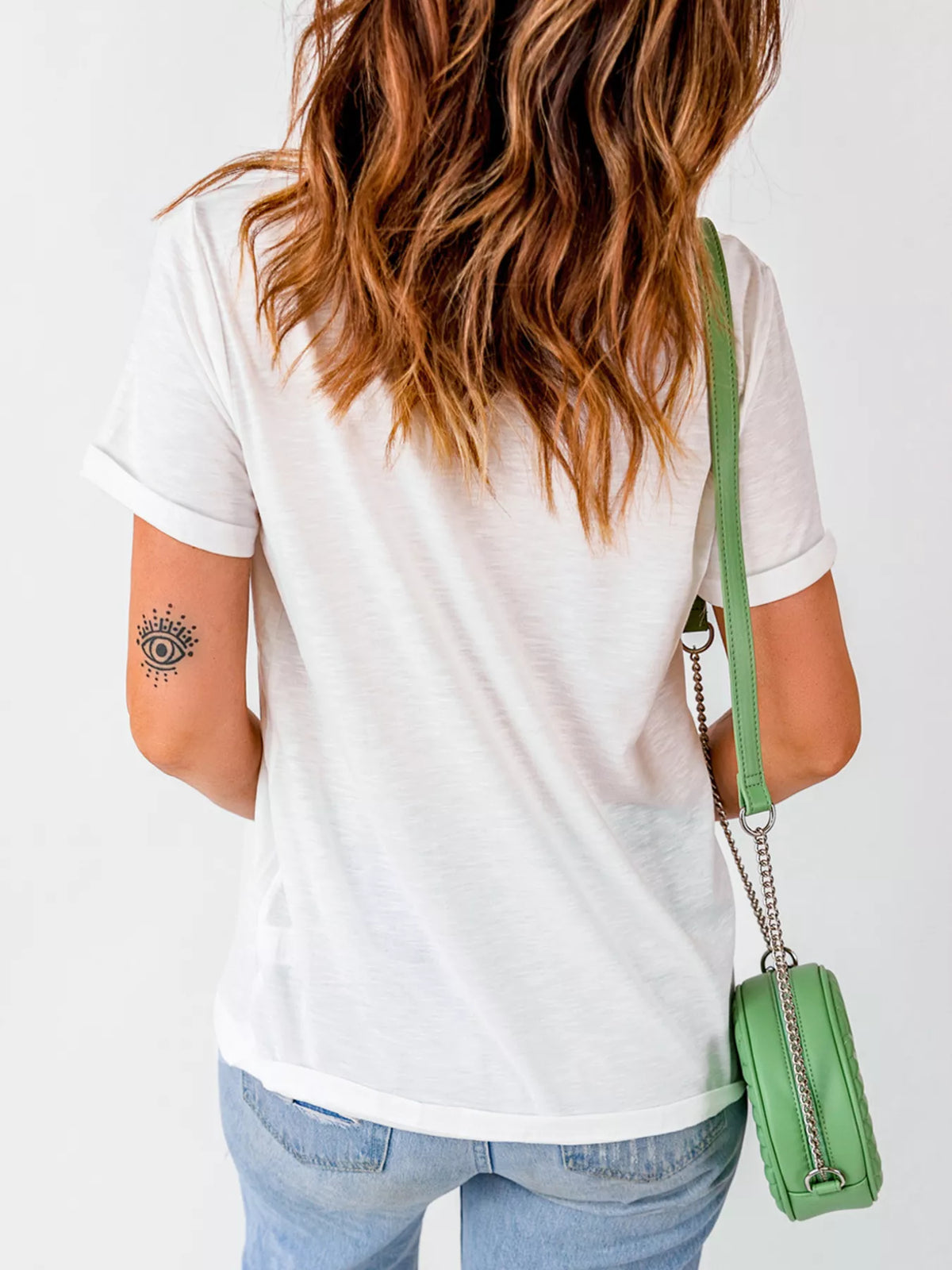 Person wearing a white t-shirt and blue jeans, carrying a green handbag on a plain background