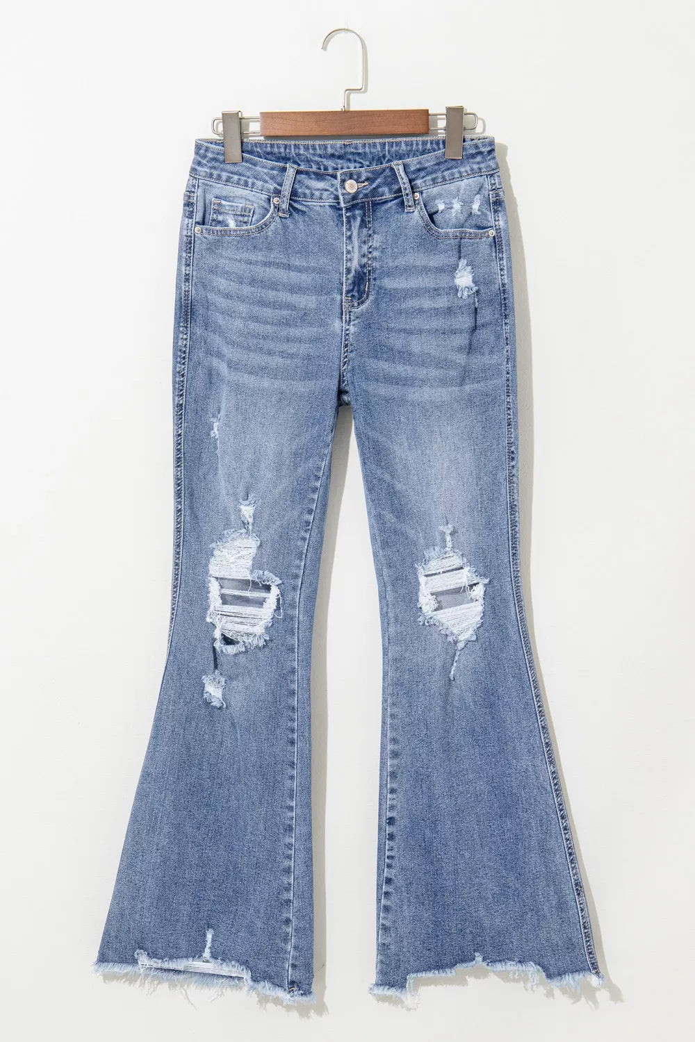 Distressed blue jeans on a hanger against a white background