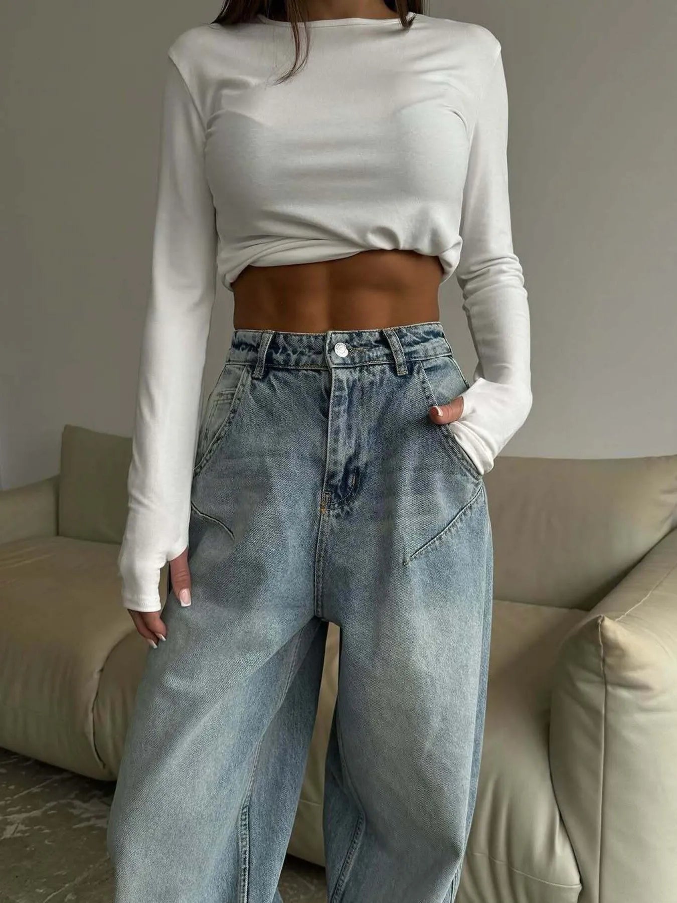 Person wearing a white long-sleeve crop top and blue jeans in a neutral setting