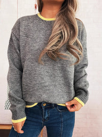 Person wearing a gray sweater with yellow trim and blue jeans against a light background