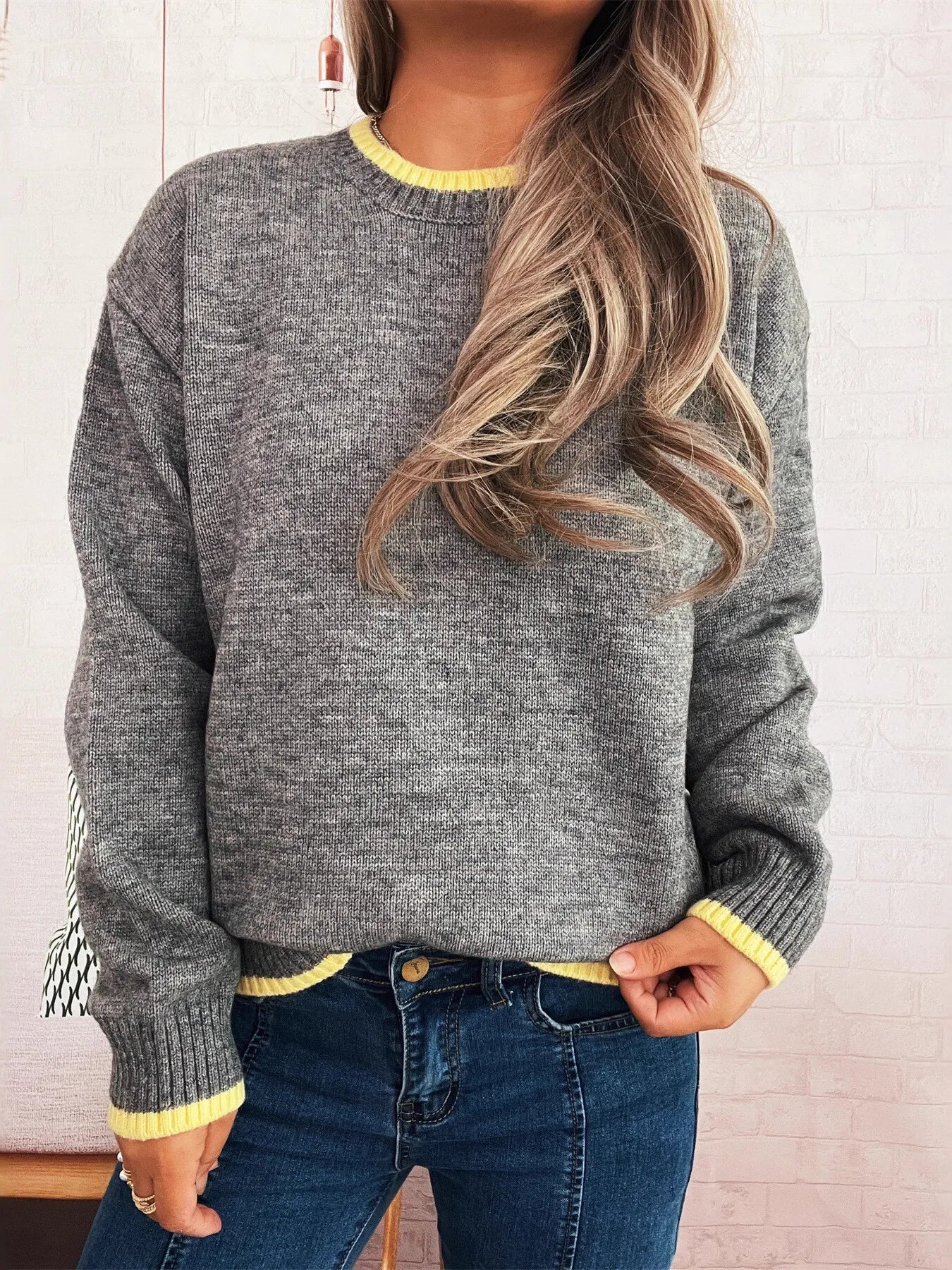 Person wearing a gray sweater with yellow trim and blue jeans against a light background