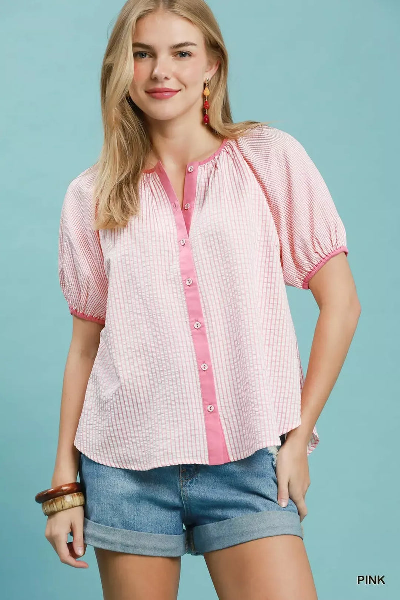 Woman wearing a pink and white checkered blouse with denim shorts on a light blue background