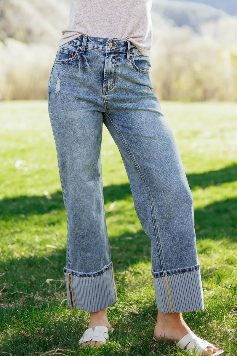 Person wearing light blue jeans standing on grass with a blurred natural background