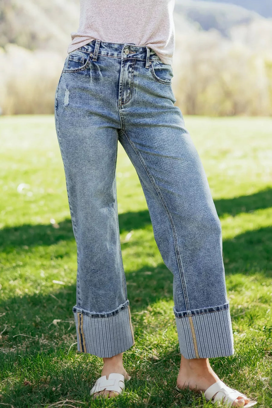 Person wearing light blue jeans standing on grass with a blurred natural background