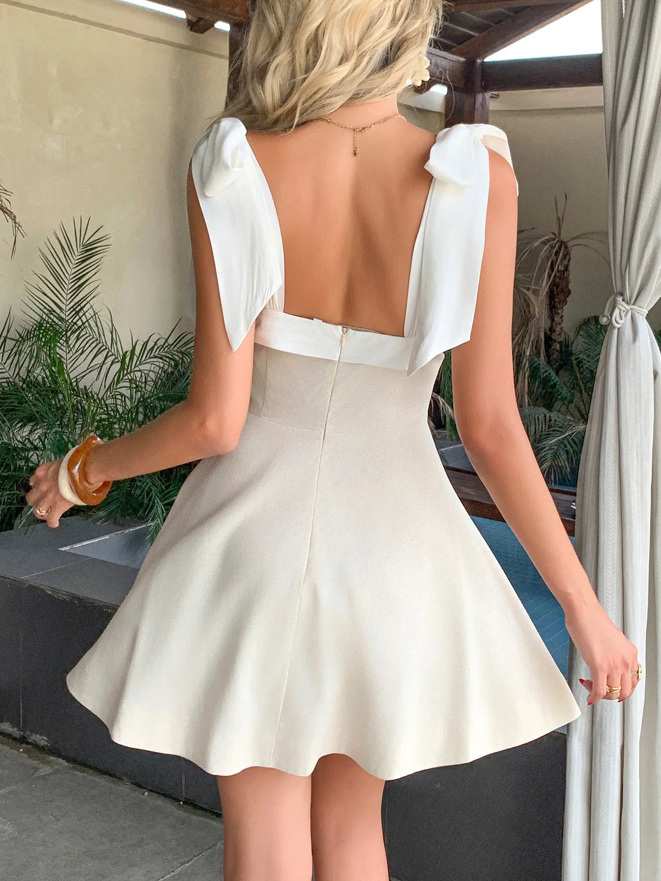 Woman wearing a white dress with a backless design, standing outdoors.