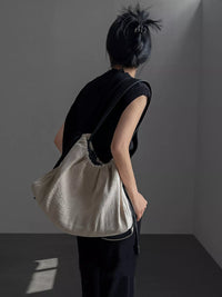 Person holding a beige textured bag against a plain background