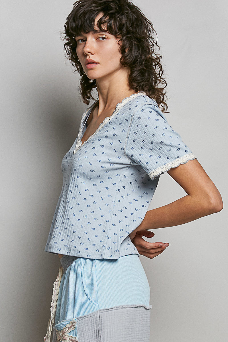 Woman wearing a light blue patterned top with lace trim against a plain background