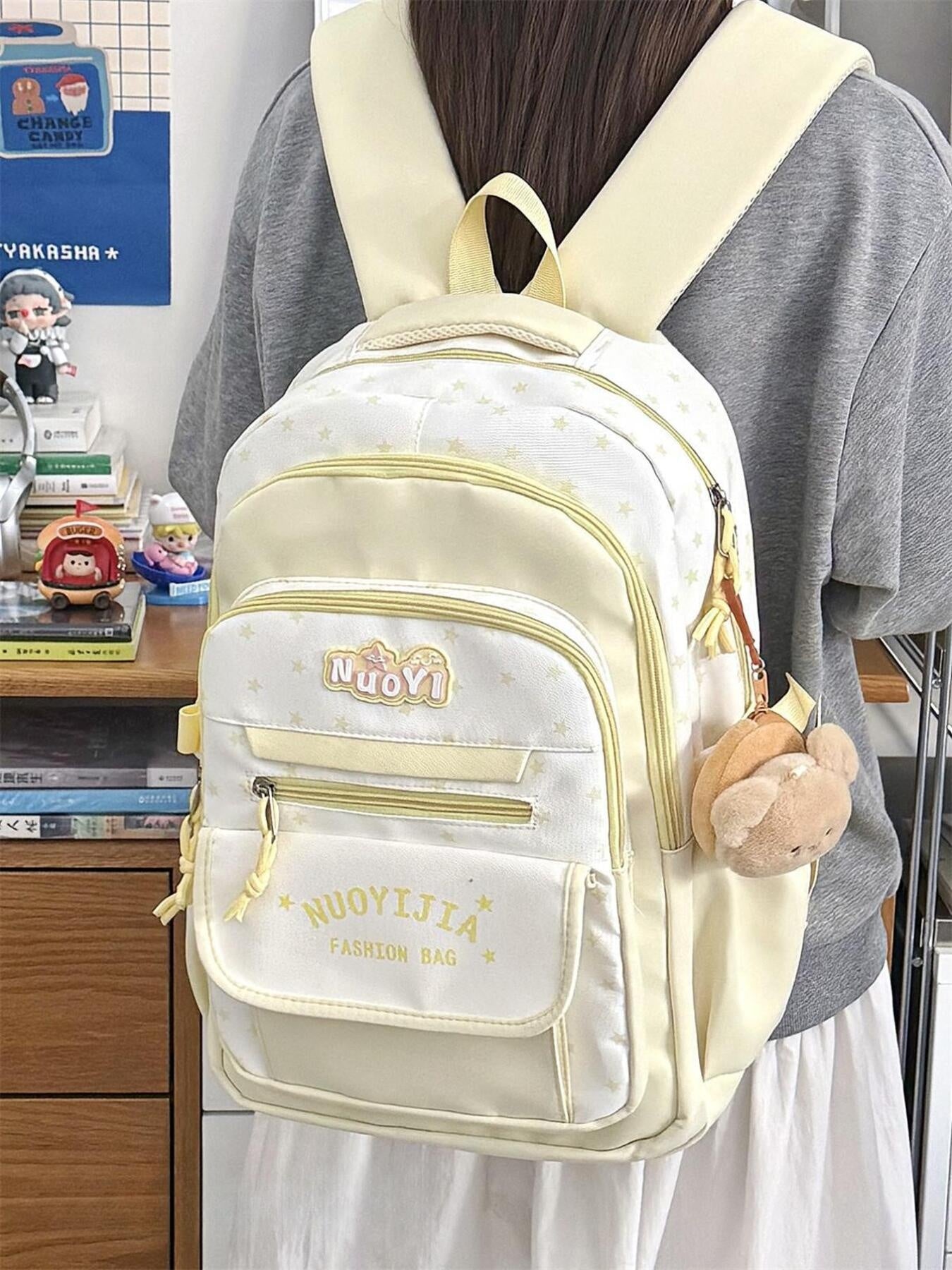 Beige backpack with gold accents worn by a person, with a blurred indoor background.