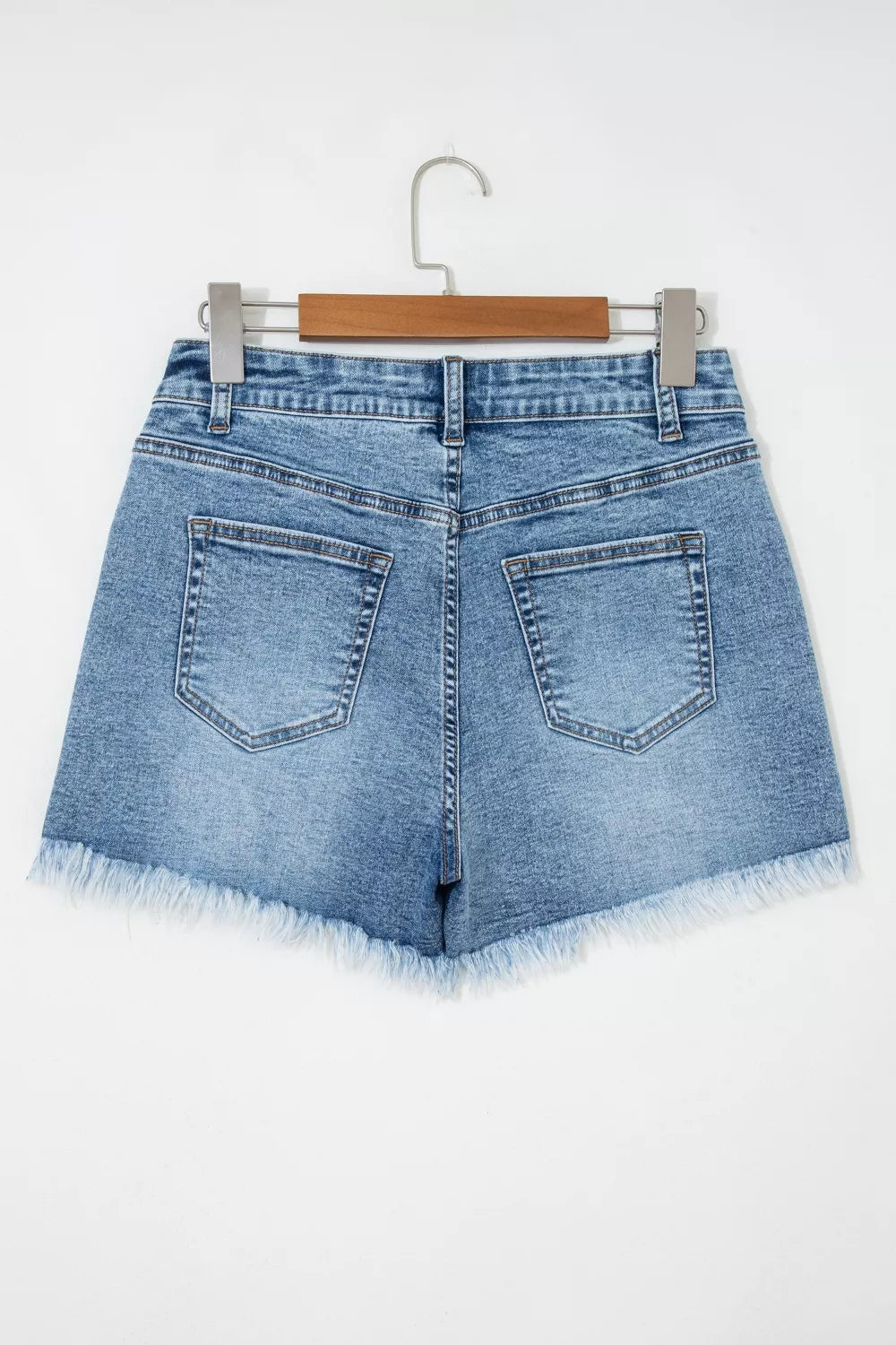 Blue denim shorts on a hanger against a white background