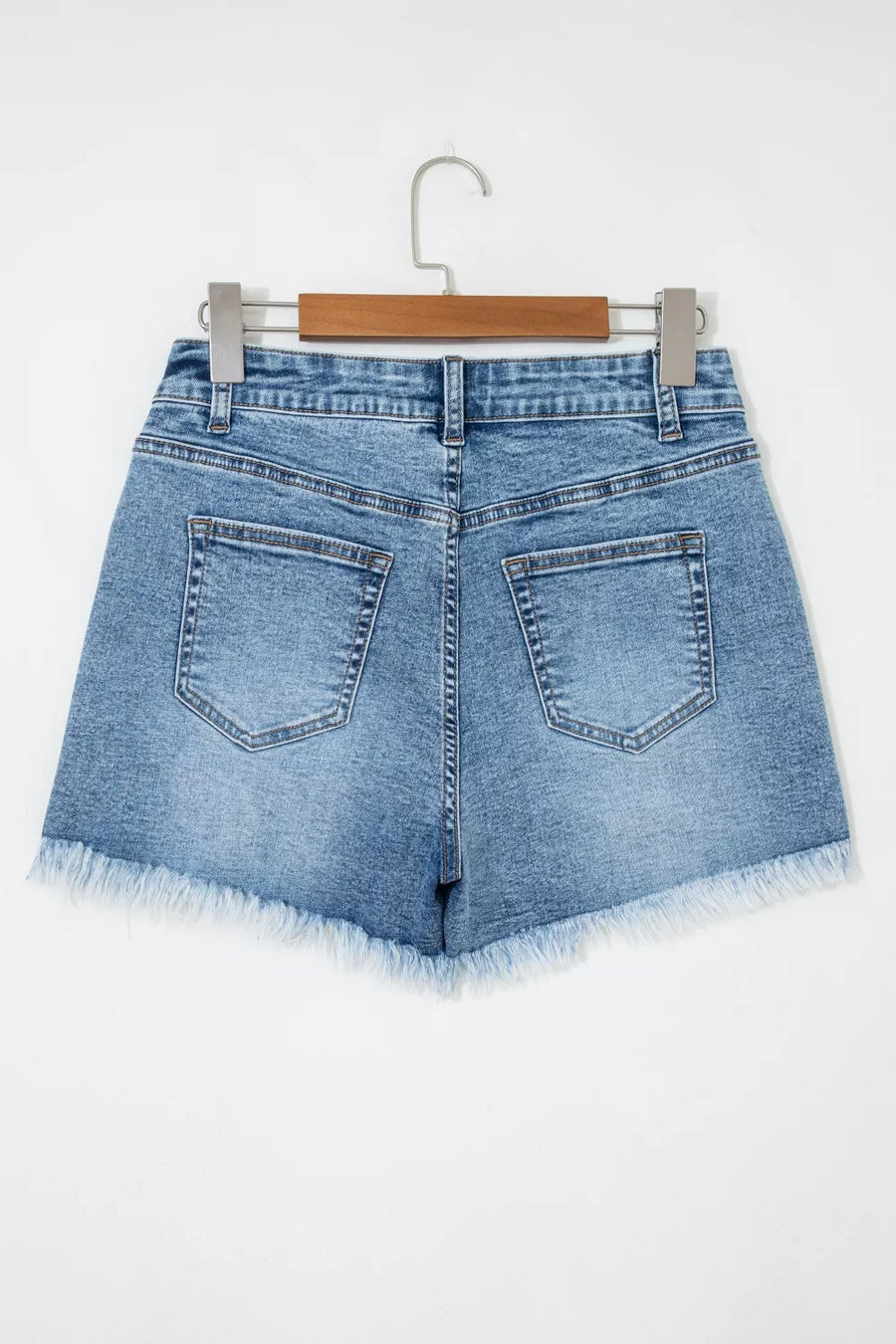 Blue denim shorts on a hanger against a white background