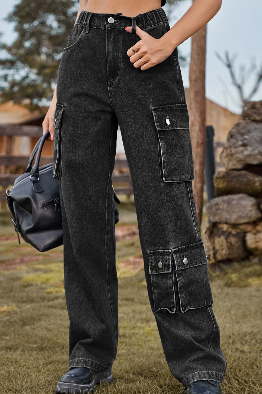 Person wearing black cargo pants holding a black bag outdoors.