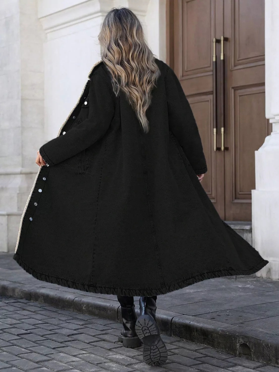 Person wearing a long black coat walking on a sidewalk.