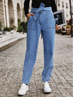 Person wearing blue jeans with a tie waist on a stone pavement.