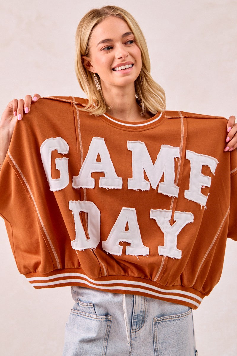 Person holding a brown sweatshirt with 'GAME DAY' text on a plain background