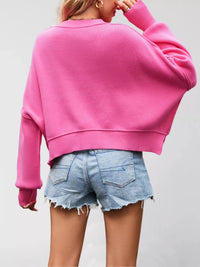 Person wearing a pink sweater and denim shorts on a plain background