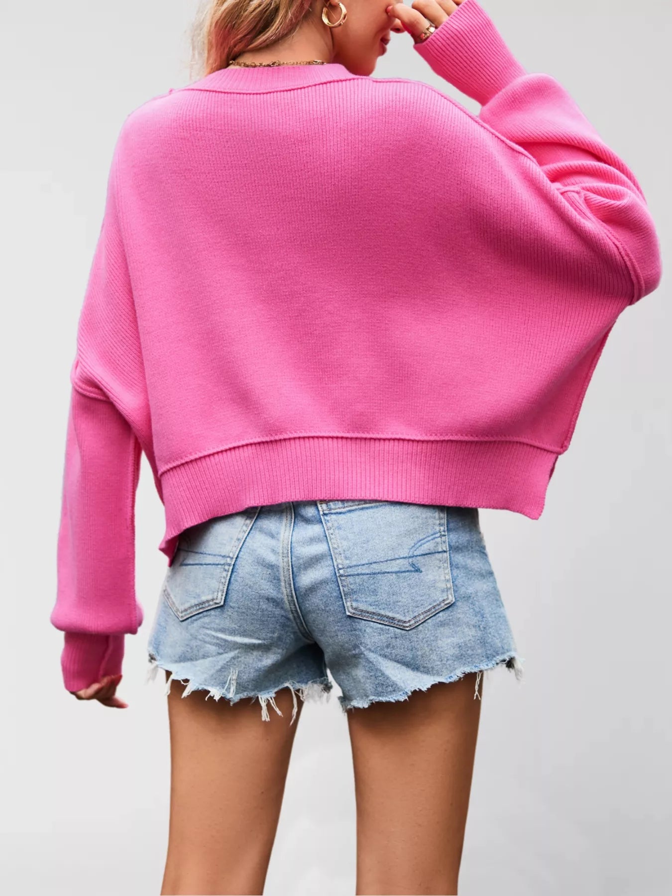 Person wearing a pink sweater and denim shorts on a plain background