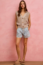 Woman wearing a sleeveless beige top and light blue shorts against a pink background