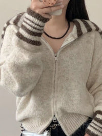 Person wearing a beige zip-up sweater with brown striped sleeves.