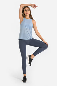 Woman in blue sleeveless top and dark leggings posing on a white background