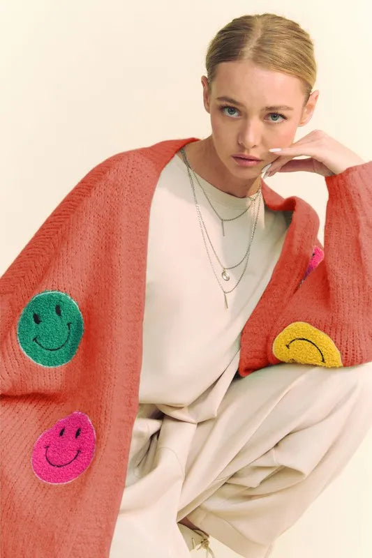 Woman wearing a red cardigan with smiley face patches on a beige background
