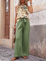 Woman wearing a floral top and green wide-leg pants standing against a textured wall.