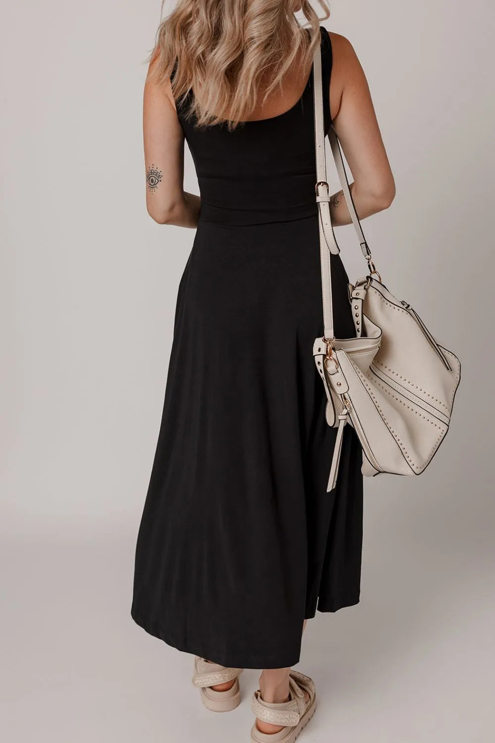 Woman in a black dress holding a beige handbag against a plain background
