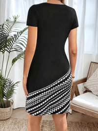 Person wearing a black dress with a patterned hem in a room with a plant and chair.