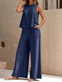 Woman wearing a navy blue sleeveless top and wide-leg pants against a beige wall.