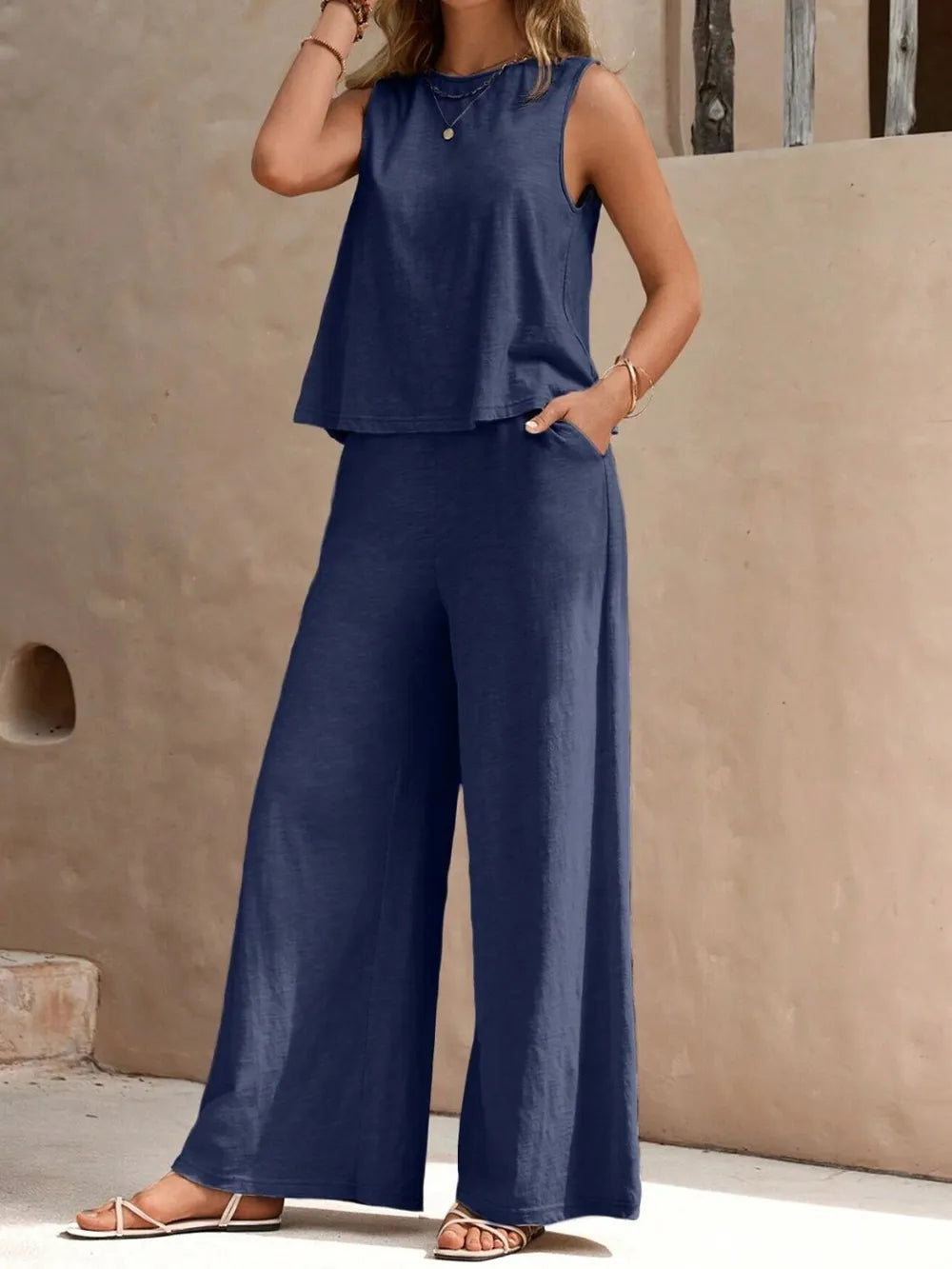Woman wearing a navy blue sleeveless top and wide-leg pants against a beige wall.