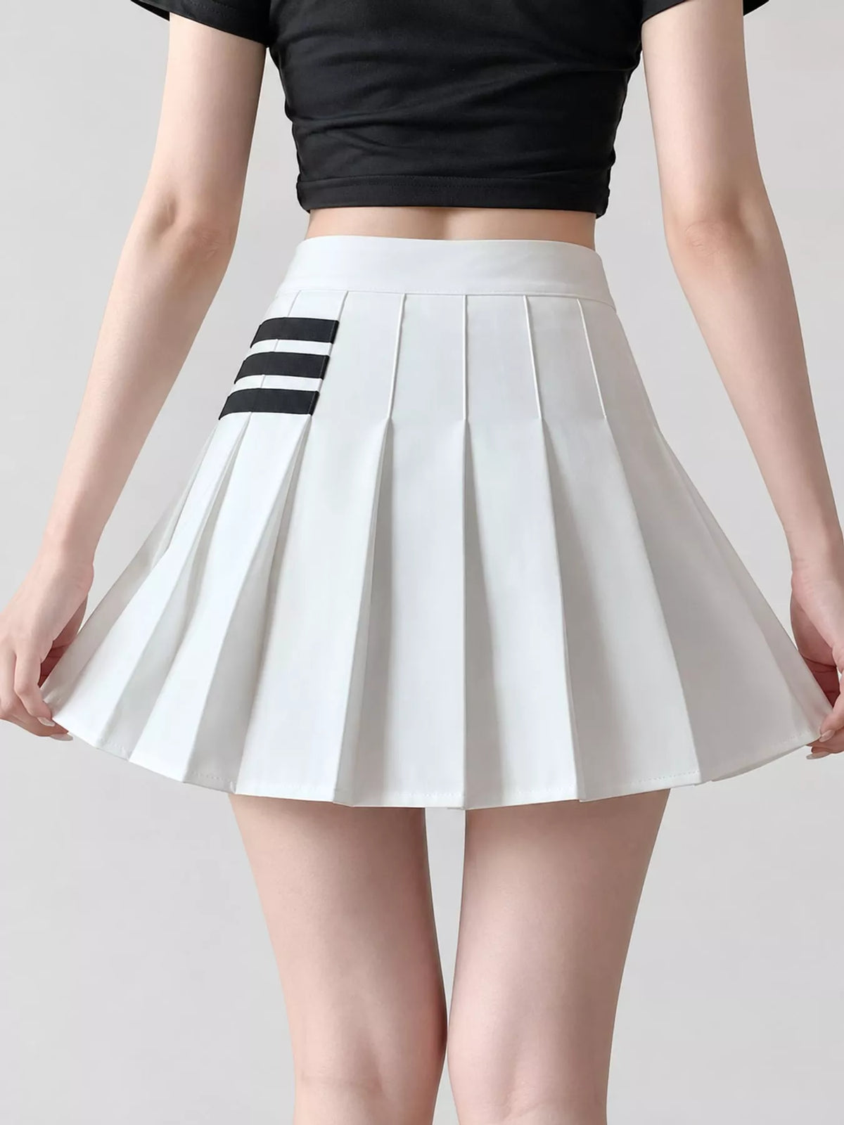 A white pleated mini skirt with three black stripes on the left side, shown on a model wearing a black crop top against a light gray background.