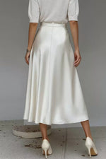 Person wearing a white skirt and high heels on a plain background