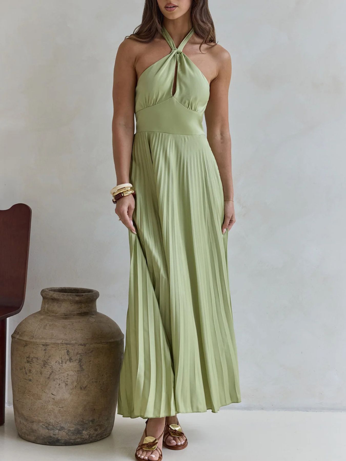 Woman wearing a light green halter neck dress standing next to a large vase against a plain background
