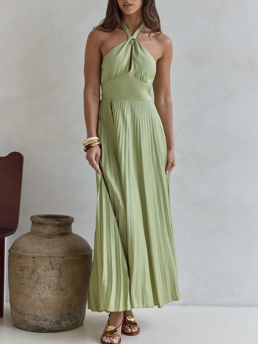 Woman wearing a light green halter neck dress standing next to a large vase against a plain background