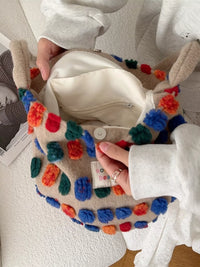 Colorful pom-pom bag held by a person wearing a white coat.